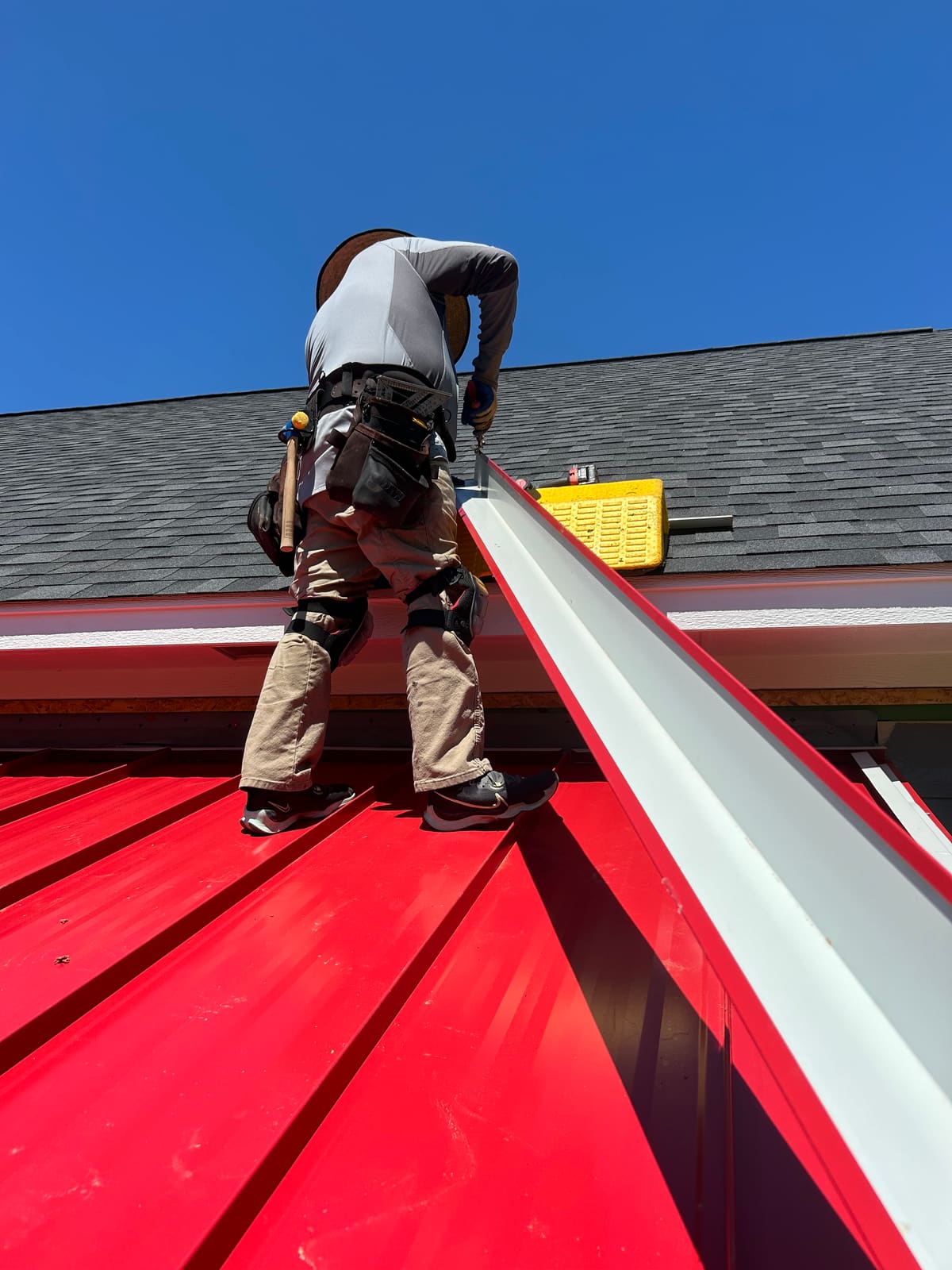 Red standing seam metal panels going on, seam by seam