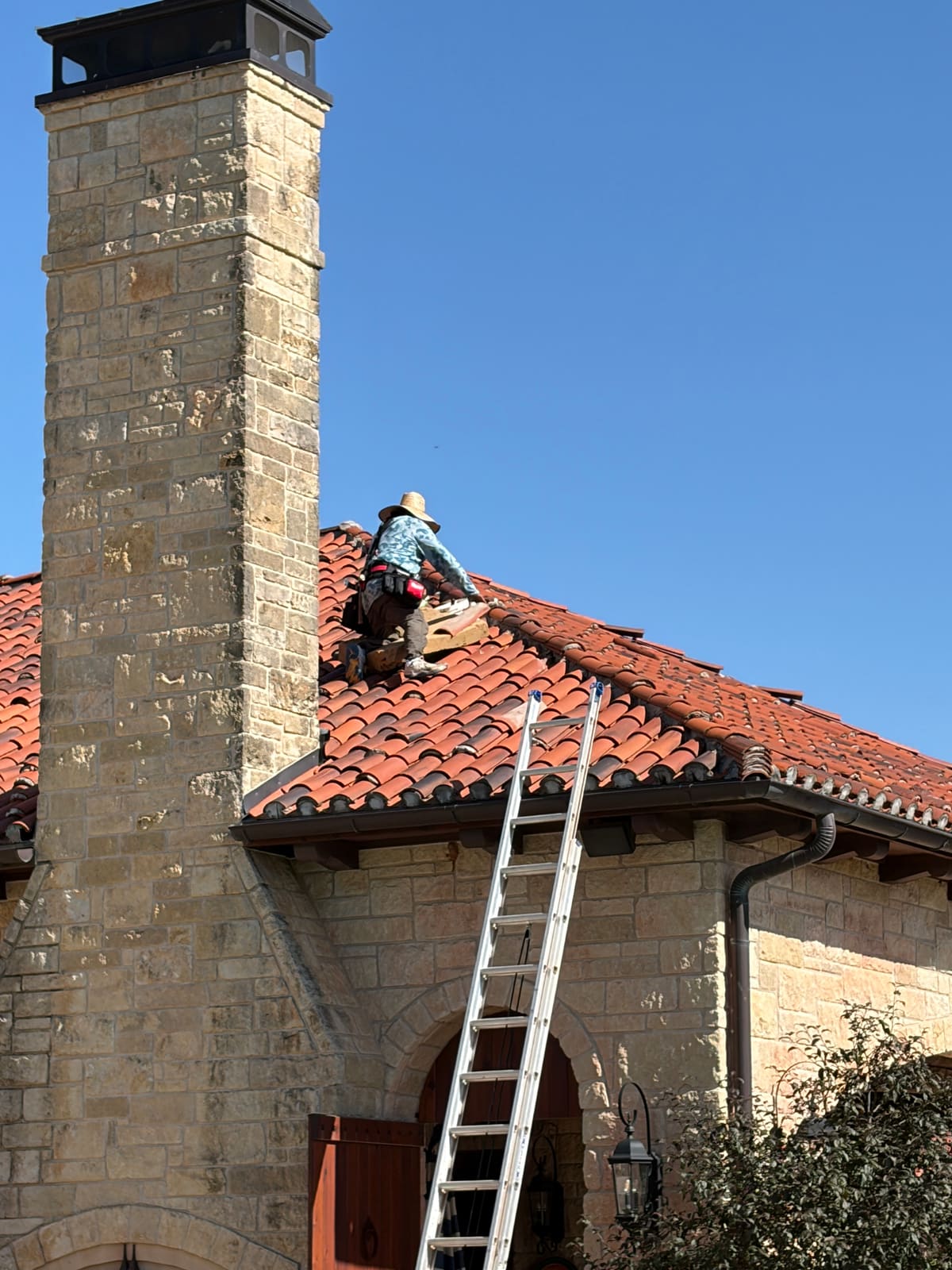 Tile repair on a stone home, chimney visible and ladder on site